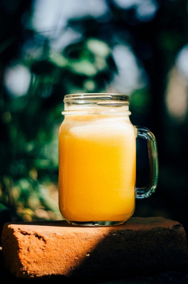 Fresh orange juice in a mason jar on a red brick, captured outdoors in daylight.